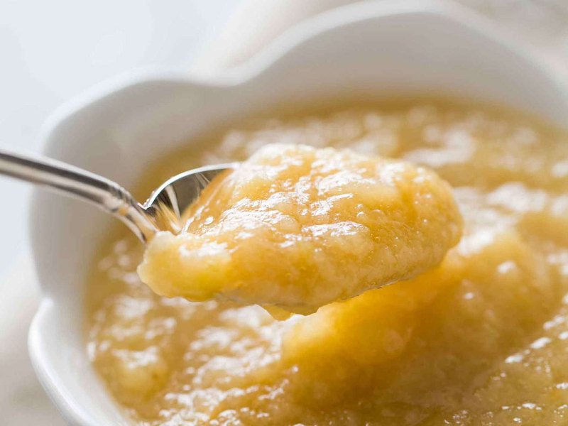 A spoonful of smooth golden apple sauce lifted from a bowl of it.