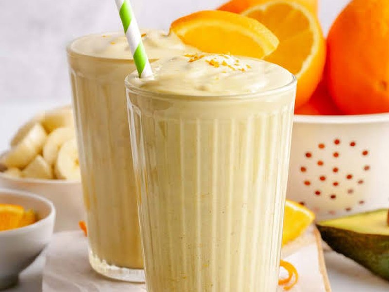 A tall glass of pale, creamy banana smoothie with a striped straw.