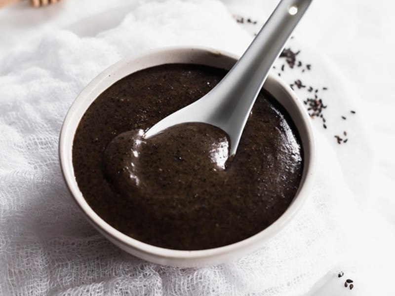 A bowl of thick, smooth black sesame soup with a spoon resting in it.