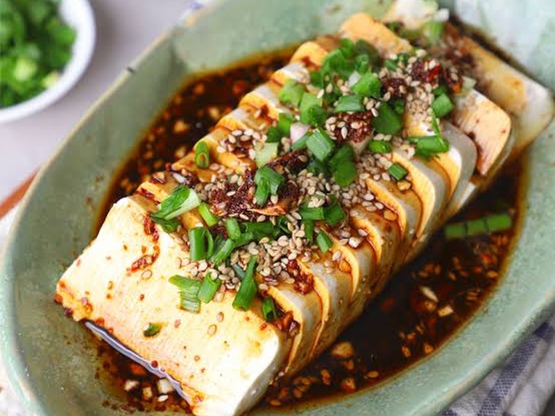 A block of silken tofu sliced into fans, topped with dark soy dressing, scallions and sesame seeds.