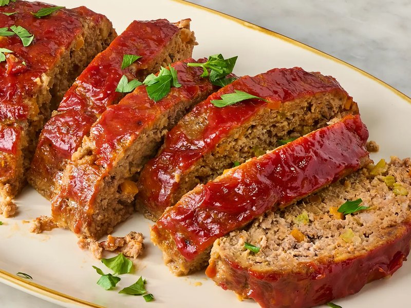 A ketchup-glazed meatloaf, sliced to show its tender interior, garnished with parsley.