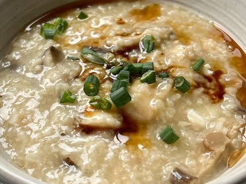 A bowl of creamy white congee topped with chopped mushroom, scallions, and a drizzle of soy and chili oil.