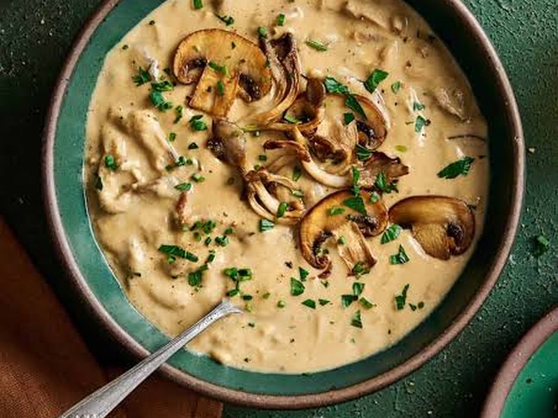 A bowl of creamy mushroom soup topped with sauteed mushroom slices and chopped parsley.
