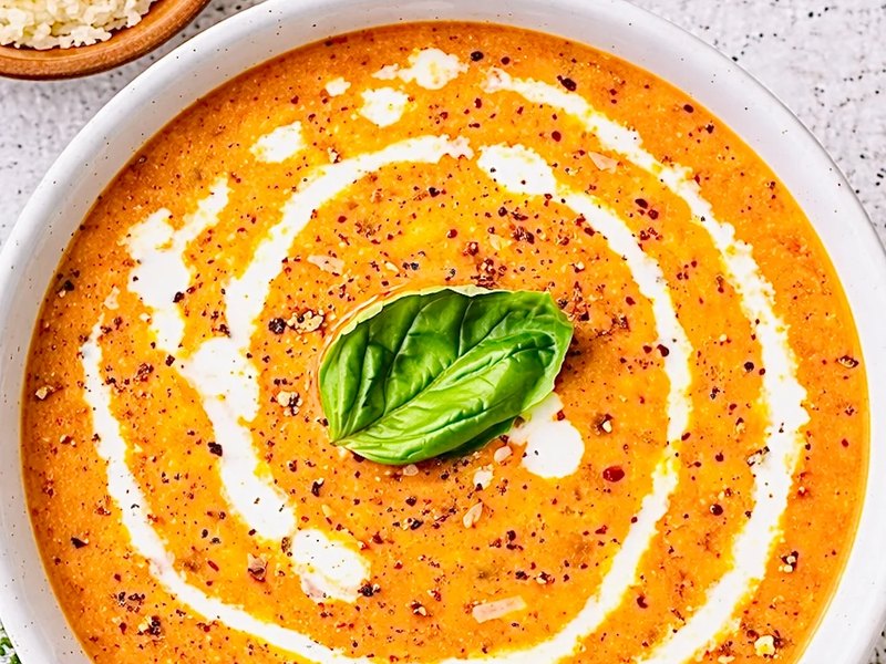 A bowl of creamy orange-red tomato soup with a swirl of cream and fresh basil.