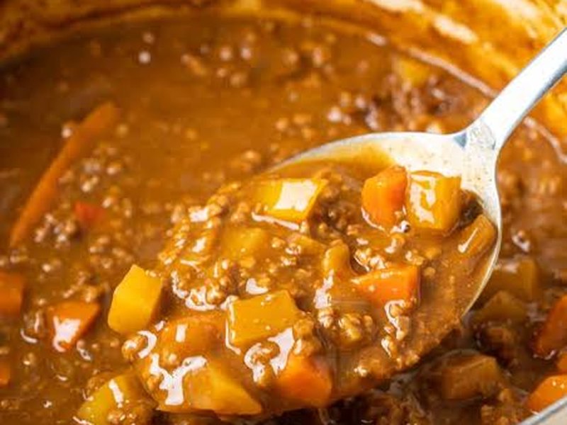 A spoonful lifted from a rich brown ground beef curry with soft potato and carrot.