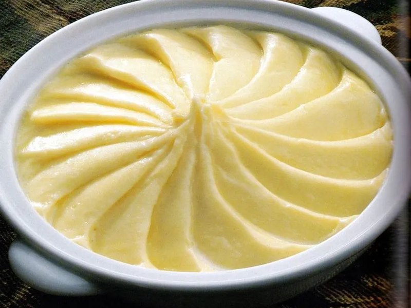 A bowl of ultra-smooth pale mashed potatoes finished with a swirled surface.
