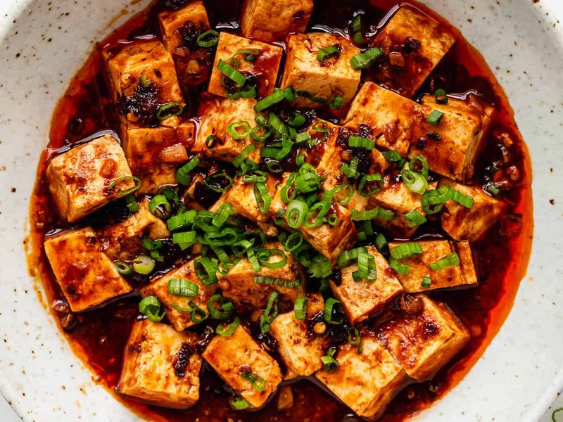 Cubes of soft tofu in a glossy red mapo sauce, scattered with chopped spring onion.