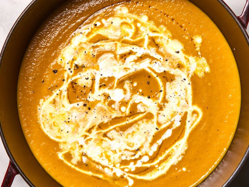 A bowl of smooth orange pumpkin soup, swirled with cream.