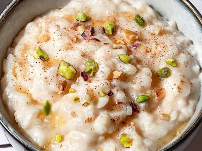 A bowl of creamy rice pudding dusted with cinnamon and scattered with chopped pistachio.