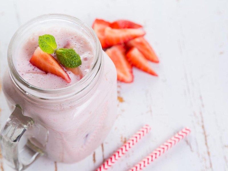 A tall glass of pale pink strawberry yogurt drink with fresh strawberries beside it.