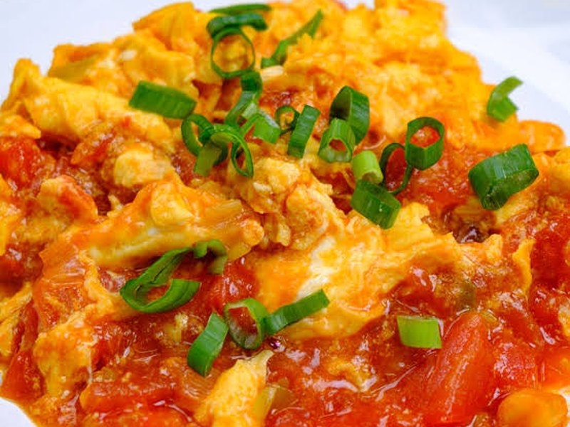 A plate of soft scrambled egg folded through tomato in a glossy orange-red sauce.