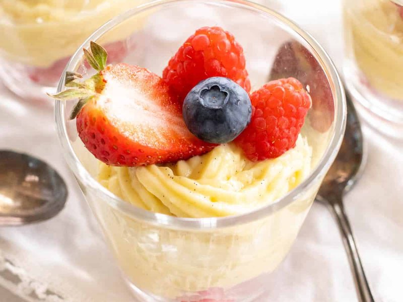 A glass of pale vanilla custard topped with fresh strawberries, raspberries and a blueberry.