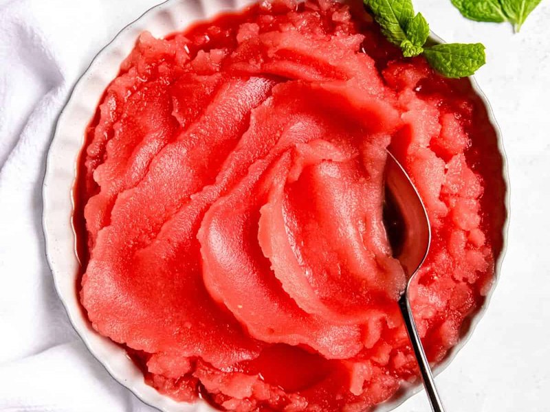 A bowl of vivid pink watermelon sorbet scooped into soft ripples, with a spoon resting in it.